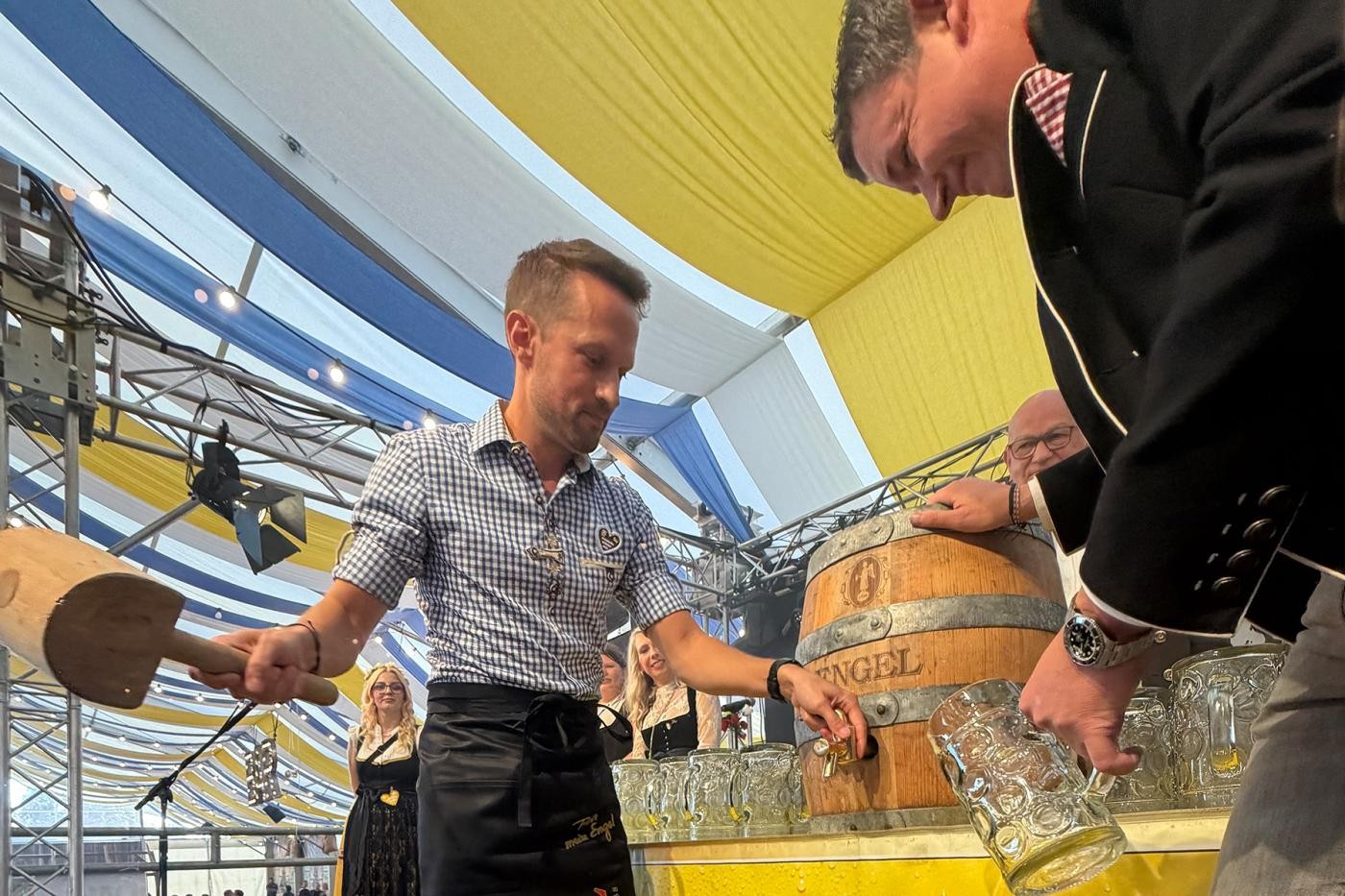Stadtverwaltung Ein Mann mit großem Holzhammer schlägt auf einen Bierhahn in einem Fass, ein anderer hält einen Krug bereit