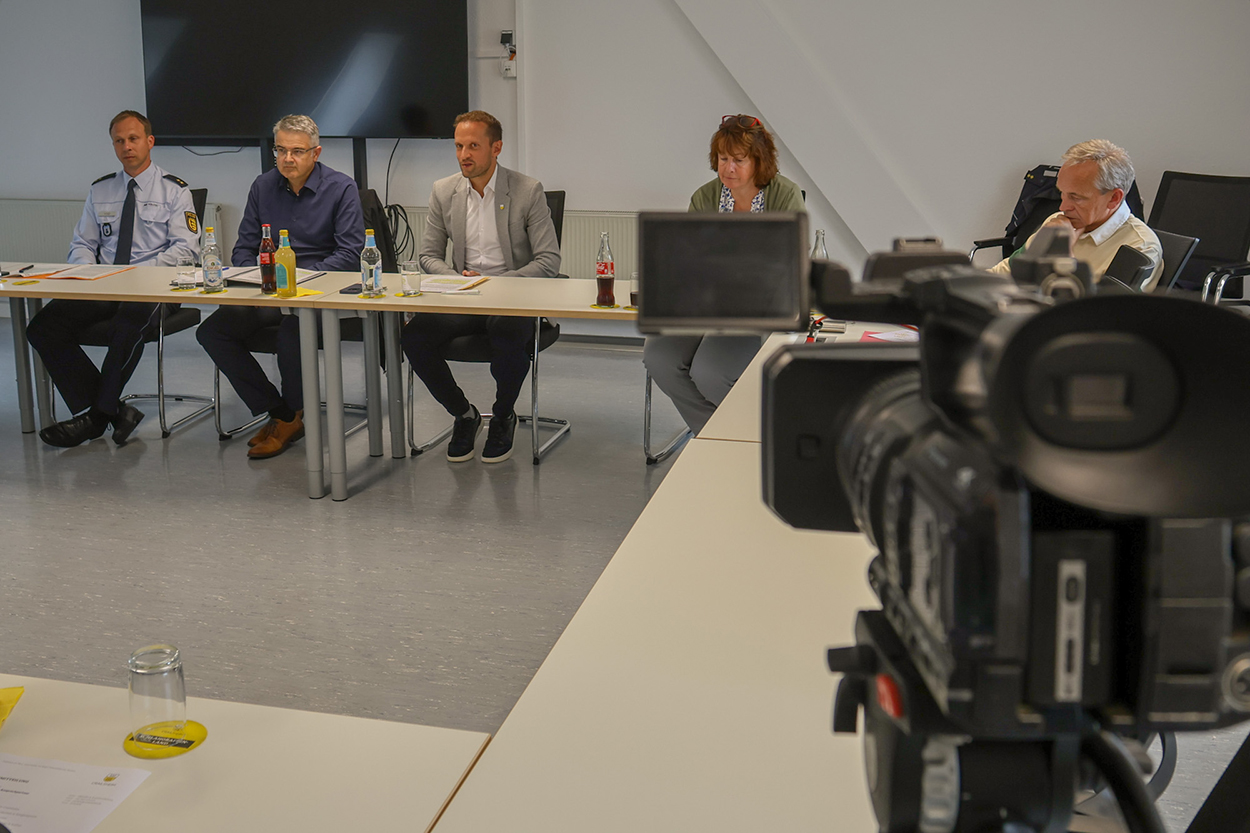 Fünf Personen sitzen hinter einem Tisch, rechts im Vordergrund ist eine Fernsehkamera zu sehen.